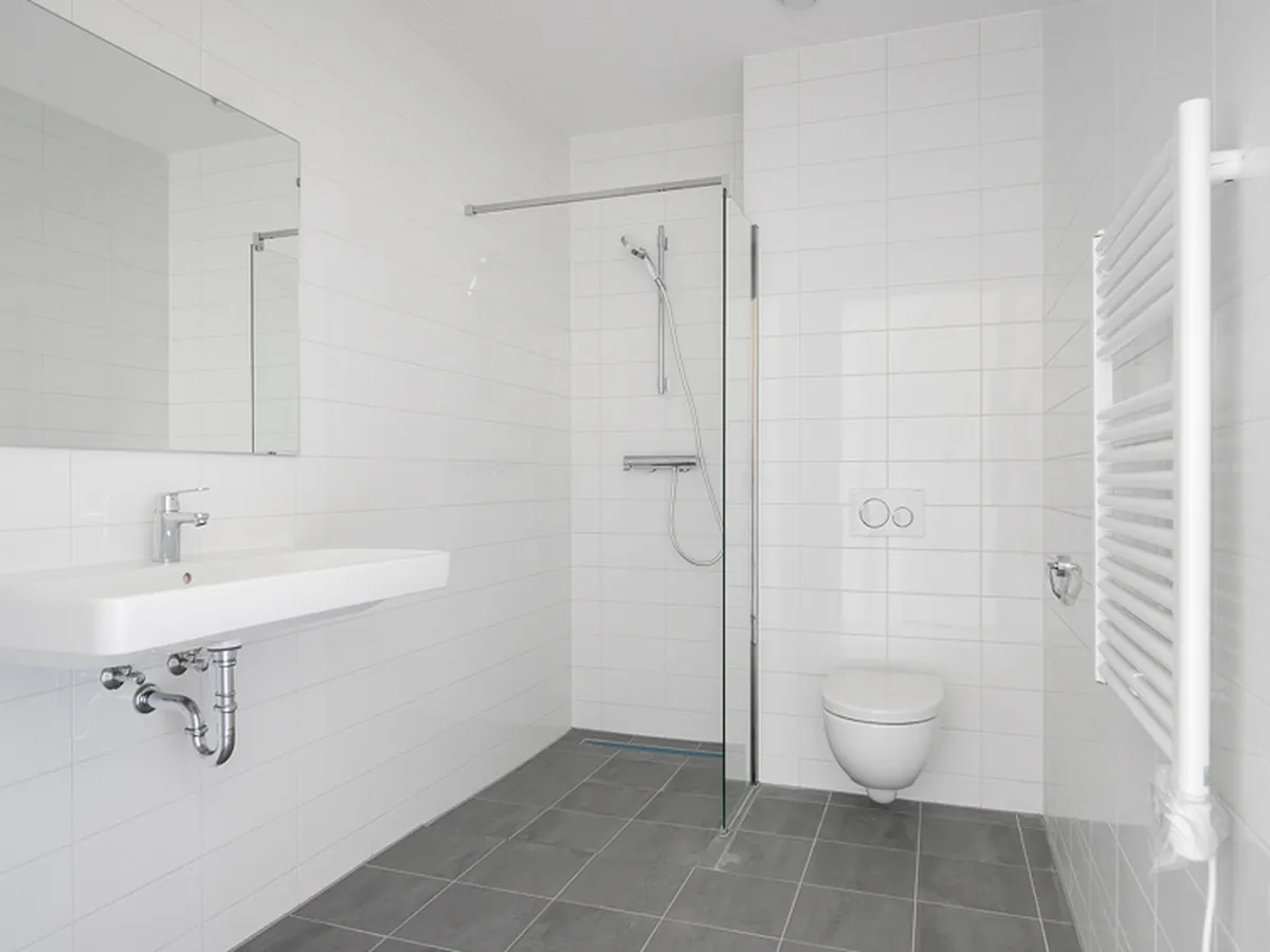 Badkamer voor de renovatie: witte wandtegels, grijze vloer en eenvoudige wastafel